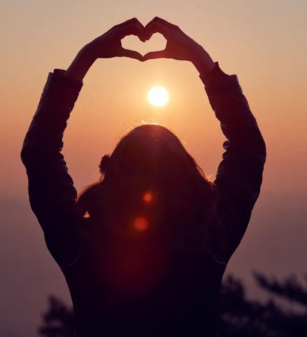 Girl Making Heart Shape Sign With Hands At Sunset